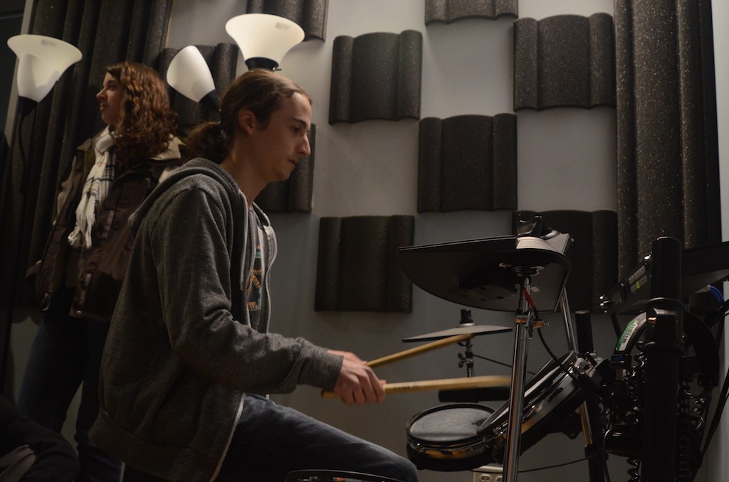 A student in a sound room sits and plays at a drum set with drum sticks.