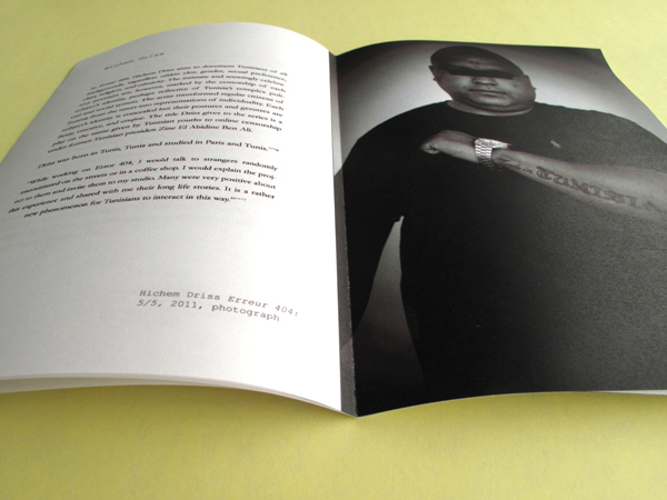 The catalog has been opened to a page with an image of a man bearing a tattoo across his arm and two paragraph texts on the other page.