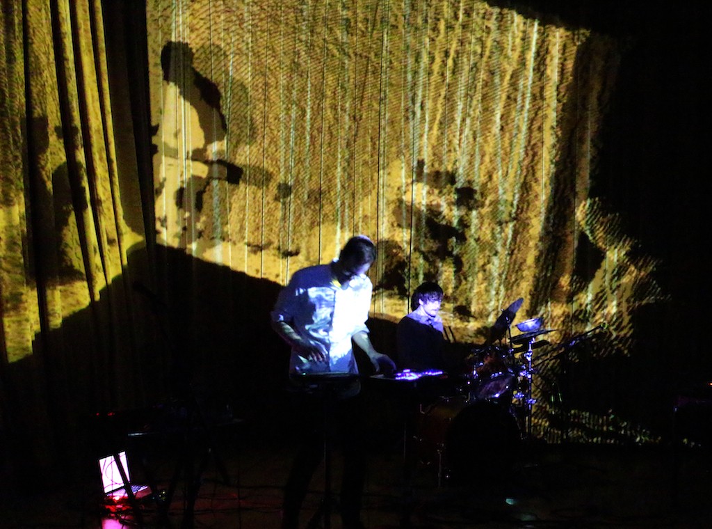 An overhead view of a man on keyboard and a drummer on a dark stage.
