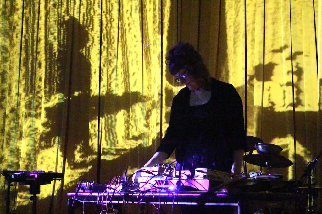 A dark-lit person with musical electronics performs on stage.
