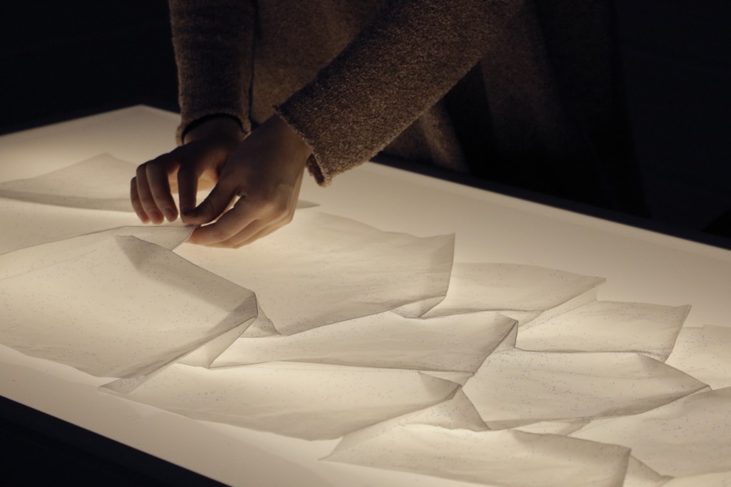 A close up of a student's hands carefully folding glassine paper over top a light box.
