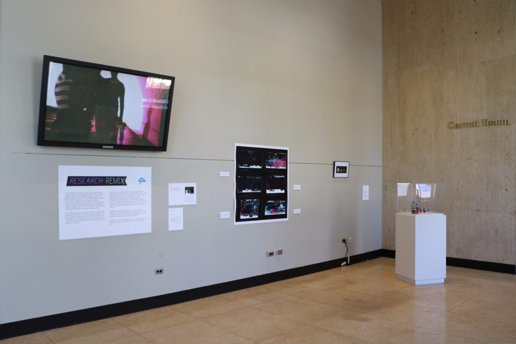 An open gallery with a monitor and three other pieces on display on the walls.