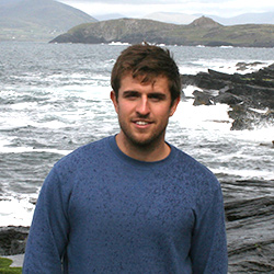 Mark standing in front of the ocean with waves crashing on rocks.