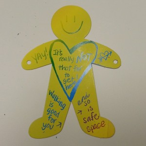 A yellow paper cut-out of a generic person with words drawn on the body and a smiley face.