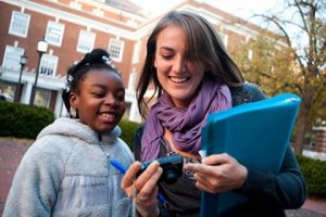 A Hopkins student and a young girl smile while looking at the display of a cell phone.