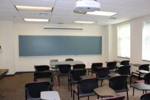 An empty classroom with individual chairs with tables facing a chalkboard in the front of the room.