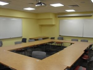 Empty classroom showing tables and chairs arranged in a rectangle. 
