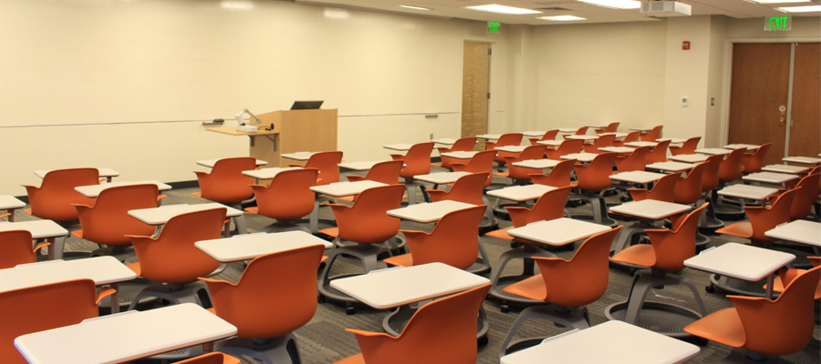A photo of the empty Krieger 170 classroom with ten rows of desks with orange chairs