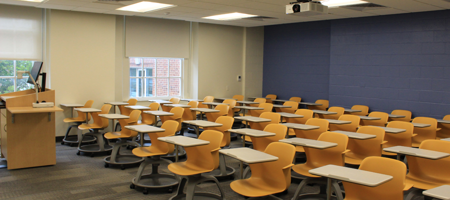 An empty Krieger 180 classroom with seven rows of desks with orange chairs