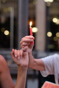 Two hands linked by pinky hold; one hand holds a lit red candle