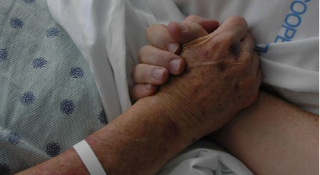 A person in a hospital bed holding another perons's hand.