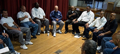 Inmates at a prison sit facing each other in a circle as they participate in a meeting