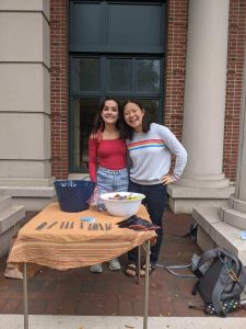 Two girls (Common Question interns) standing side-by-side in front of the pop-up table for the CQ National Coming Out Day celebration.