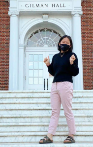 Zandy Wong standing in front of Gilman Hall, wearing a black sweater, pink pants, and sandals.