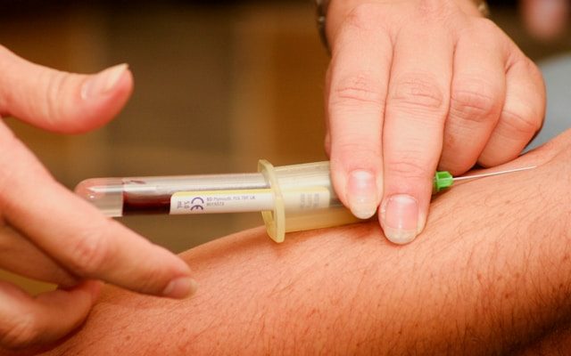 A closeup image of a phlebotomist taking a vial of blood from the arm of a patient.