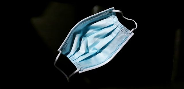 A blue paper medical mask on a black background.