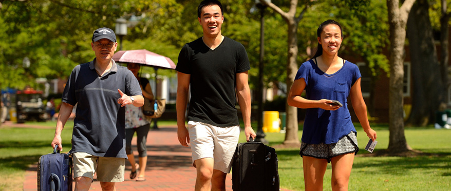 Student walking across campus with luggage