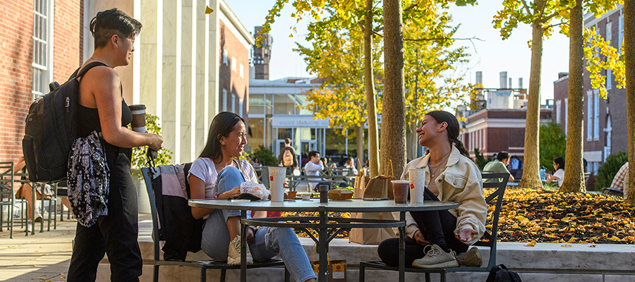 Three students smile while chatting at a table in front of the MSE Library