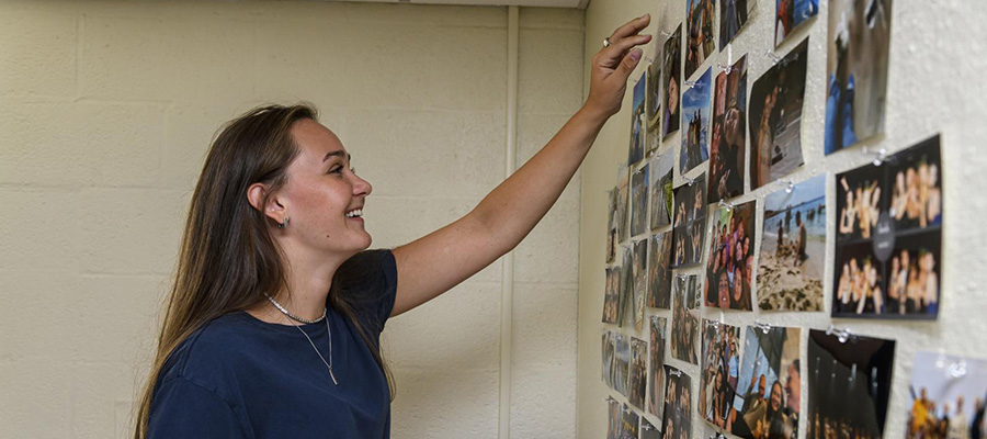 A student smiles as she arranges photos on the wall in her residence hall