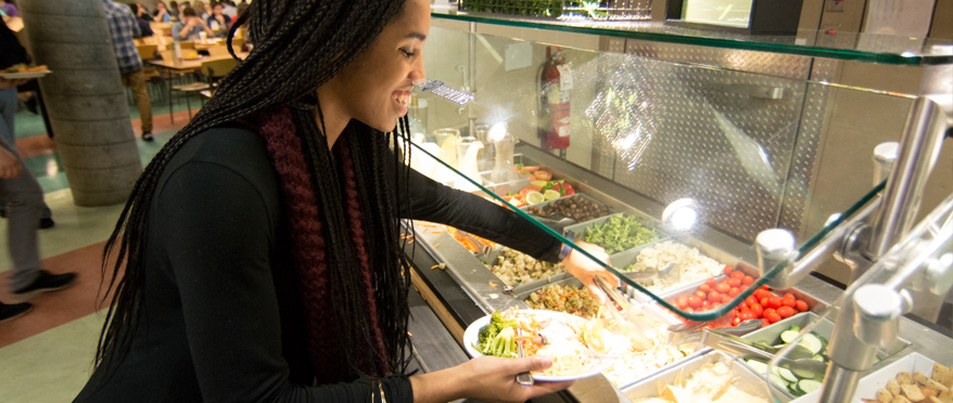 A student smiling while picking food from a buffet to place on their plate.
