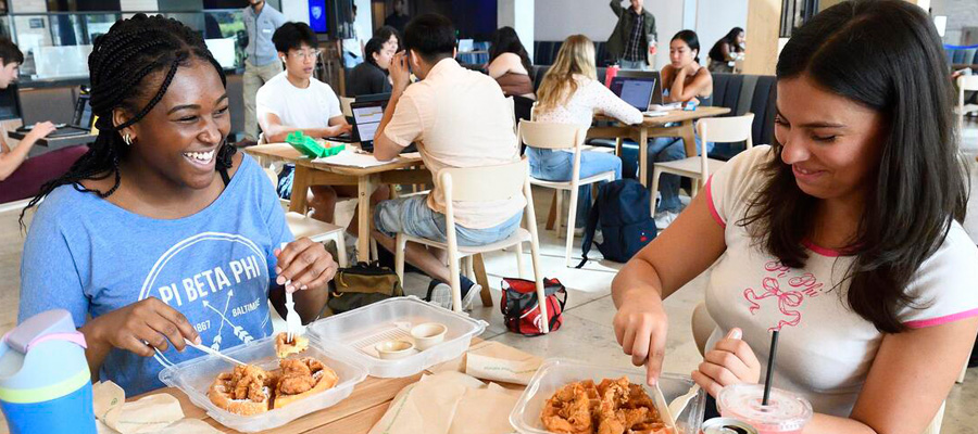 Two students eating food while laughing.