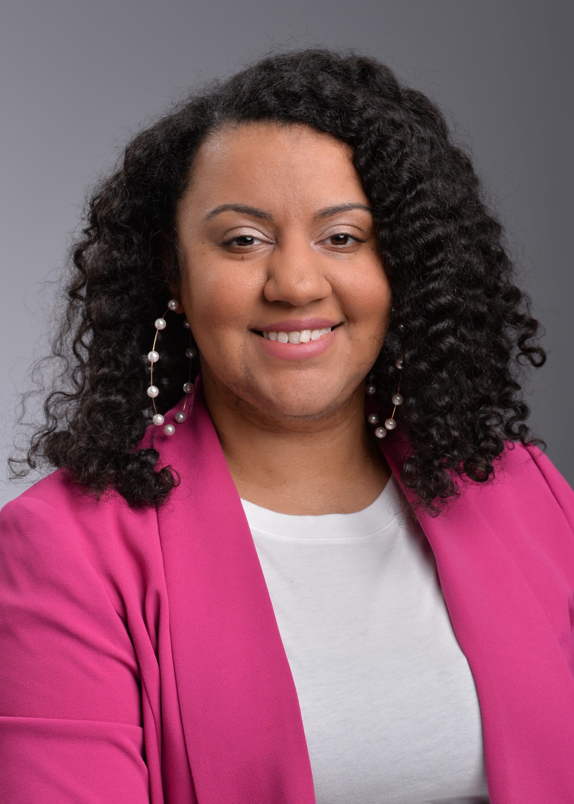 Black woman with shoulder length curly hair and a bright pink jacket.