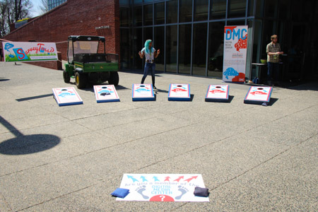 Outdoor shot of DMC SurveyToss‽ in Mattin Center courtyard with six cornhole boards, starting point, bean bags and banners in background