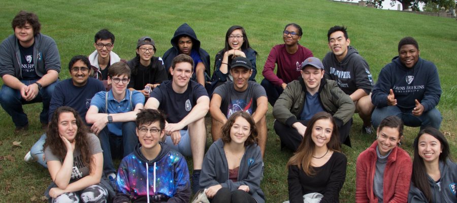 A group of students sit on the lawn and smile for a picture.