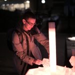 A student adds their personalized disk to the art sculpture highlighted in white light.