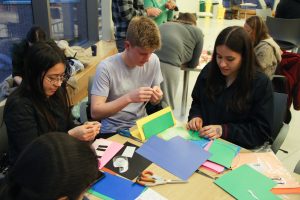 Three students at a table with colored construction paper around them while they craft with paper.