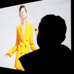 A black shadow of a man looking at a woman in a yellow dress on the screen.