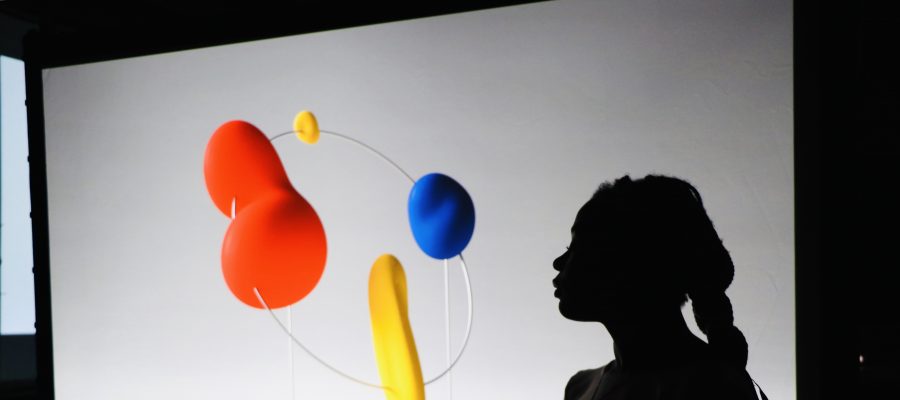Artwork that includes a woman's shadow and red, blue, and yellow objects wired together with a thin piece.