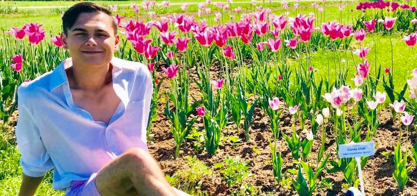 Ian Markham sits on the ground next to a garden of pink flowers.