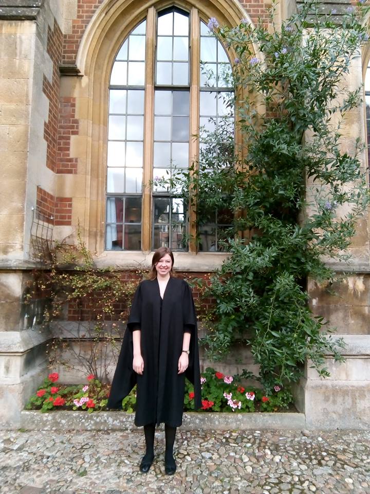 Katherine Robinson stands on a cobble stone street in front of a beautiful arched window.