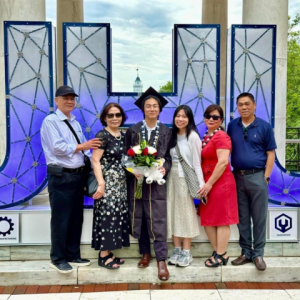 Family photo of Hopkins student Taylor Nguyen at graduation. They are standing in front of giant blue letters that spell out, "JHU."