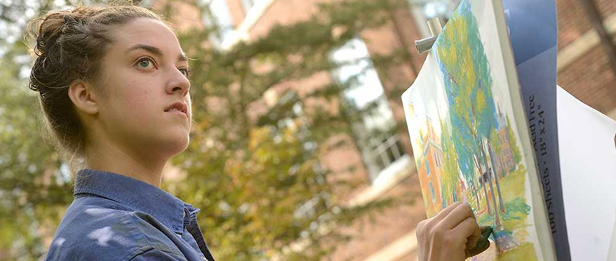 A close-up of a woman looking out toward the distance as she draws in color the landscape.