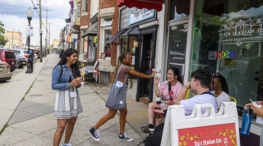 A group of students sit at a cafe table outside of an Italian Ice shop on the Avenue in Hampden