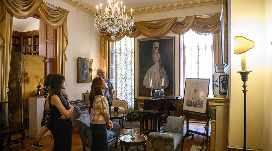 A group of students listen to a docent-led tour in a formal sitting room in the Homewood Museum