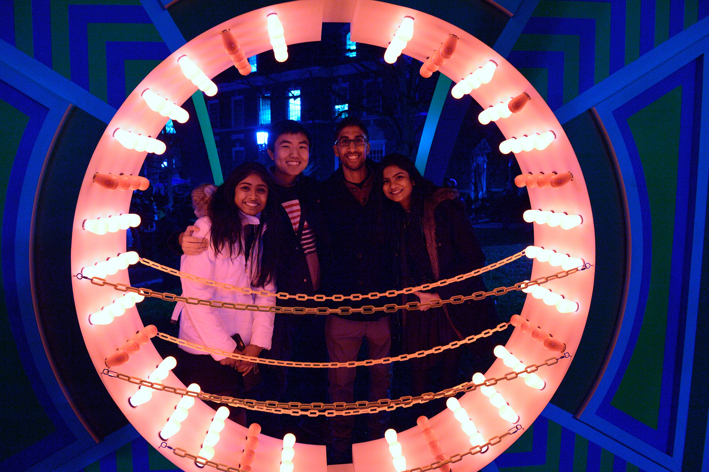 Four students posing for a photo, illuminated by a lighted sculpture by Scott Pennington.