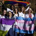 A group of people hold the trans flag, genderqueer flag, and pride flag