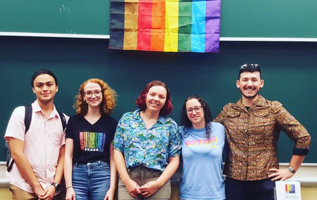 Five students standing under a rainbow flag.