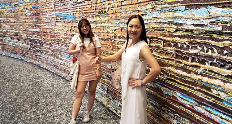 Carol Lu and her mother, Katie Yan Yue Loo, stand in front of an art wall at a museum
