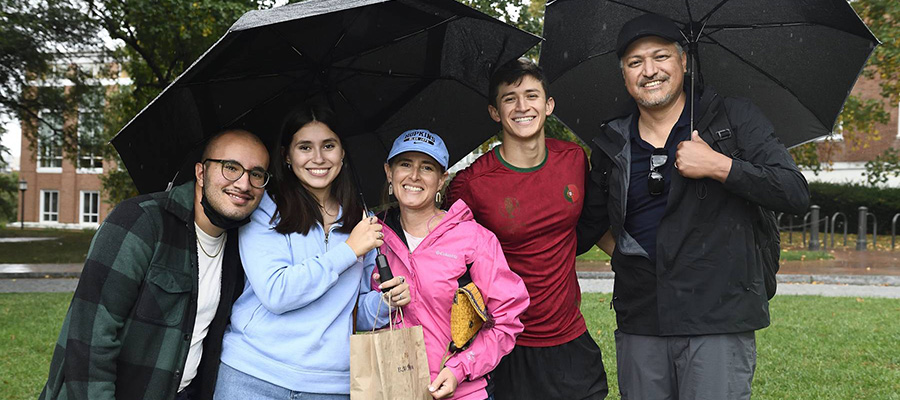 A student and her family members pose for a photo on campus during Family Weekend, holding umbrellas