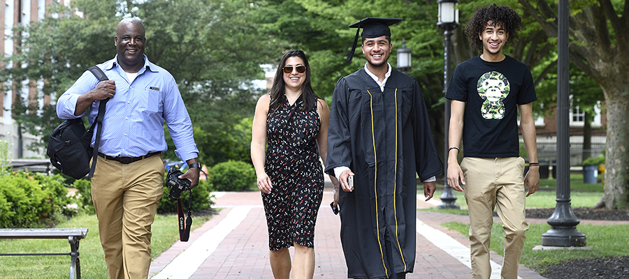 Two parents walk with their sons, one of whom is wearing graduation regalia, on JHU's campus