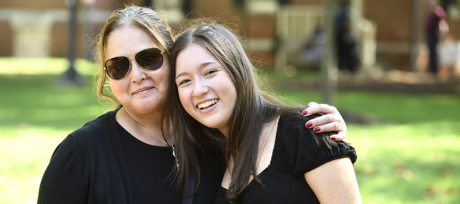 A mother wearing sunglasses hugs her daughter on JHU's campus