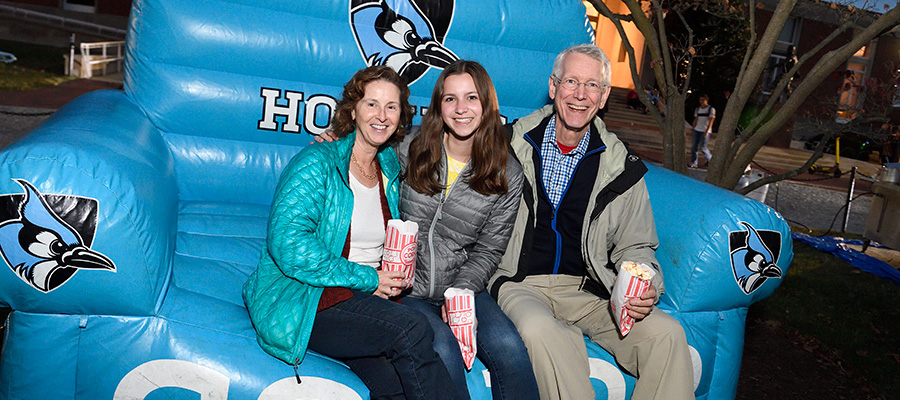 A student and her parents sit on an inflatable couch while holding popcorn