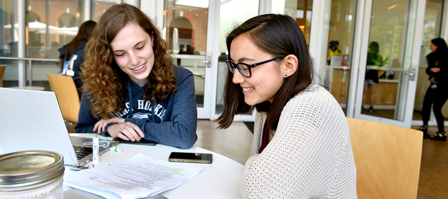 Two students sit at a table in the MSE Library and smile while looking at a printed resume
