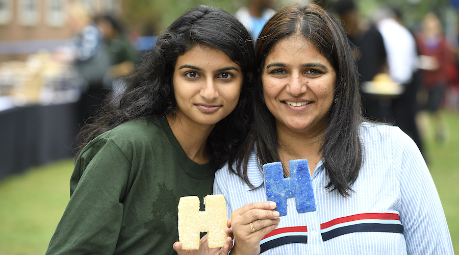 A student and her mother hold up H-shaped sugar cookies for a photo during a Parent and Family Weekend event