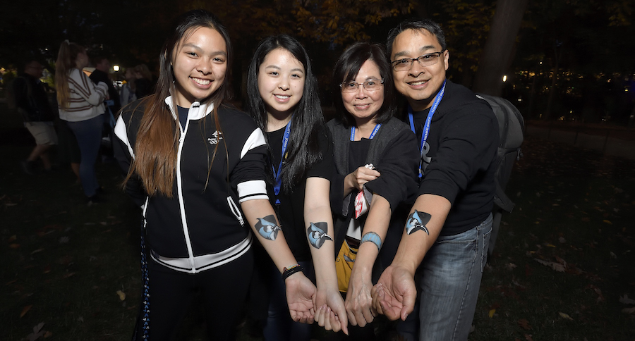 Students and their parents display temporary Blue Jay tattoos on their arms at a Parent and Family Weekend event