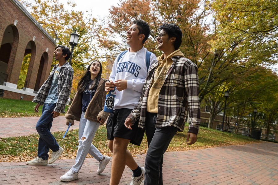 4 happy students walk together outside on campus.